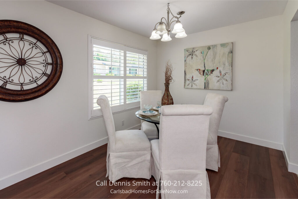 Dining area at 4414 Chickadee Way Oceanside Home for Sale with round glass table, four upholstered chairs, wall art, and bright natural light from window.