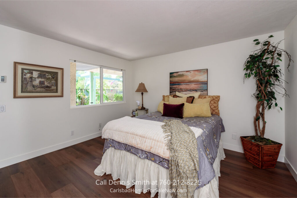 Cozy bedroom at 4414 Chickadee Way Oceanside Home for Sale featuring hardwood floors, large window with natural light, and a queen bed with layered pillows.