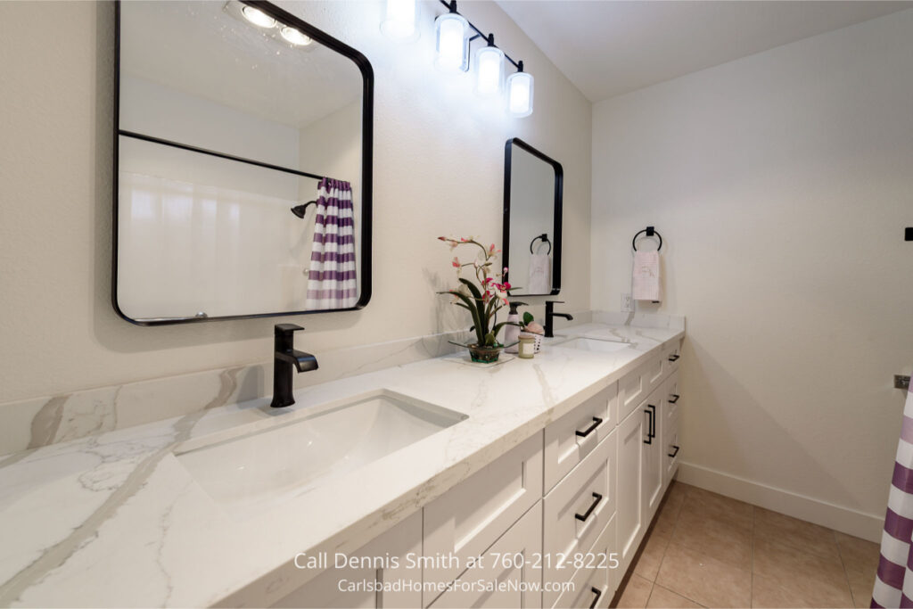 Modern bathroom inside 4414 Chickadee Way Oceanside Home for Sale with dual sinks, marble-style countertops, black fixtures, and framed mirrors.