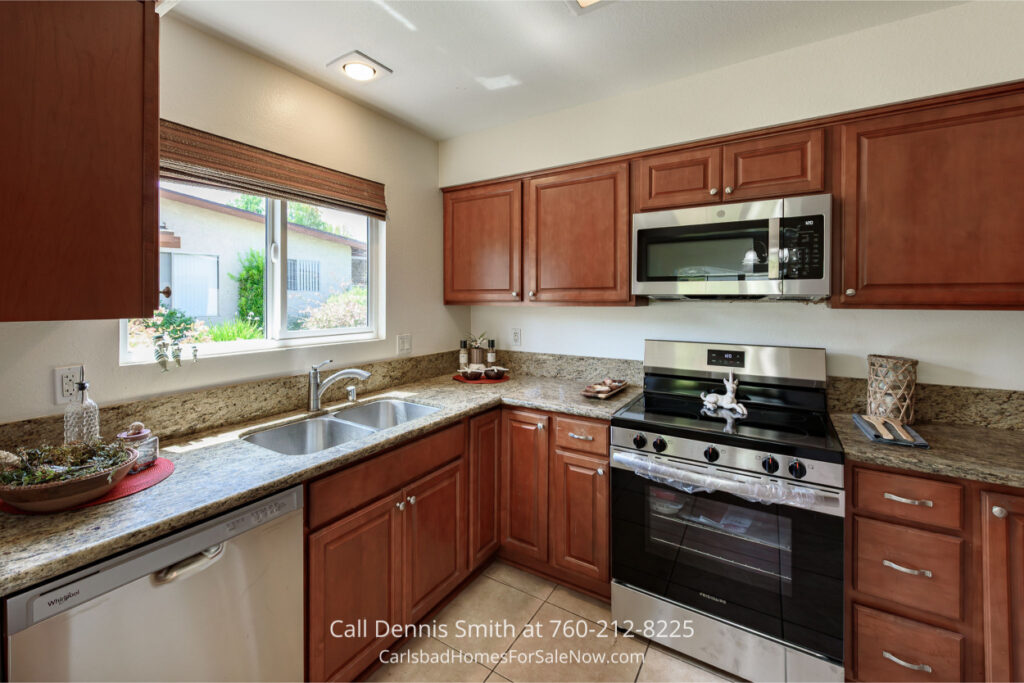 Upgraded kitchen inside 4414 Chickadee Way Oceanside Home for Sale with granite countertops, wood cabinets, stainless steel appliances, and bright window.
