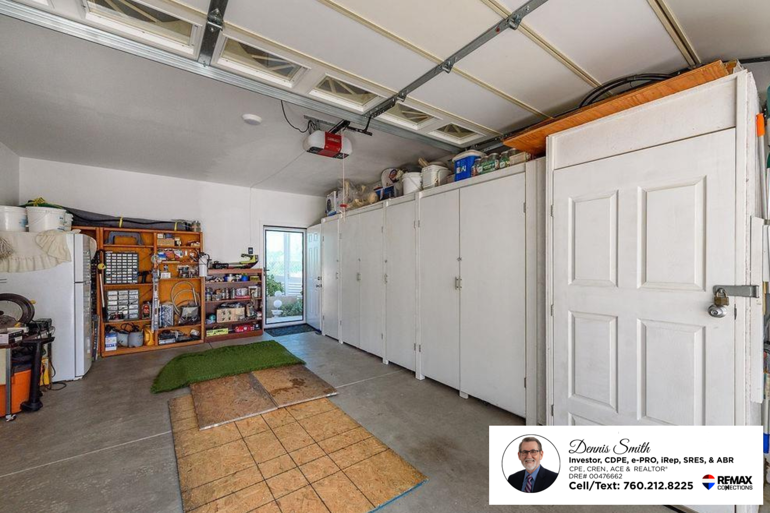 Spacious attached garage with built in white storage cabinets, shelving for tools and supplies, overhead garage door, and extra workspace ideal for hobbies, organization, and everyday storage needs.